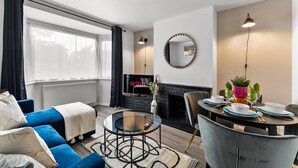 A modern living room with a sofa, a coffee table, a fireplace, and a dining area with a table set for four.
