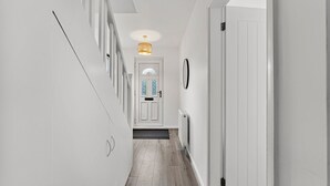 A narrow hallway with white walls, a wooden floor, and a door at the end.
