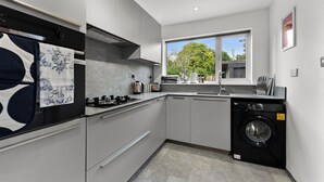 A modern kitchen with grey cabinets, a built-in washing machine, and a window providing a view of trees.