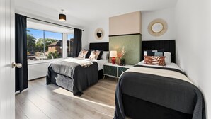 A modern hotel room with two beds, a large window, and a view of the outside.
