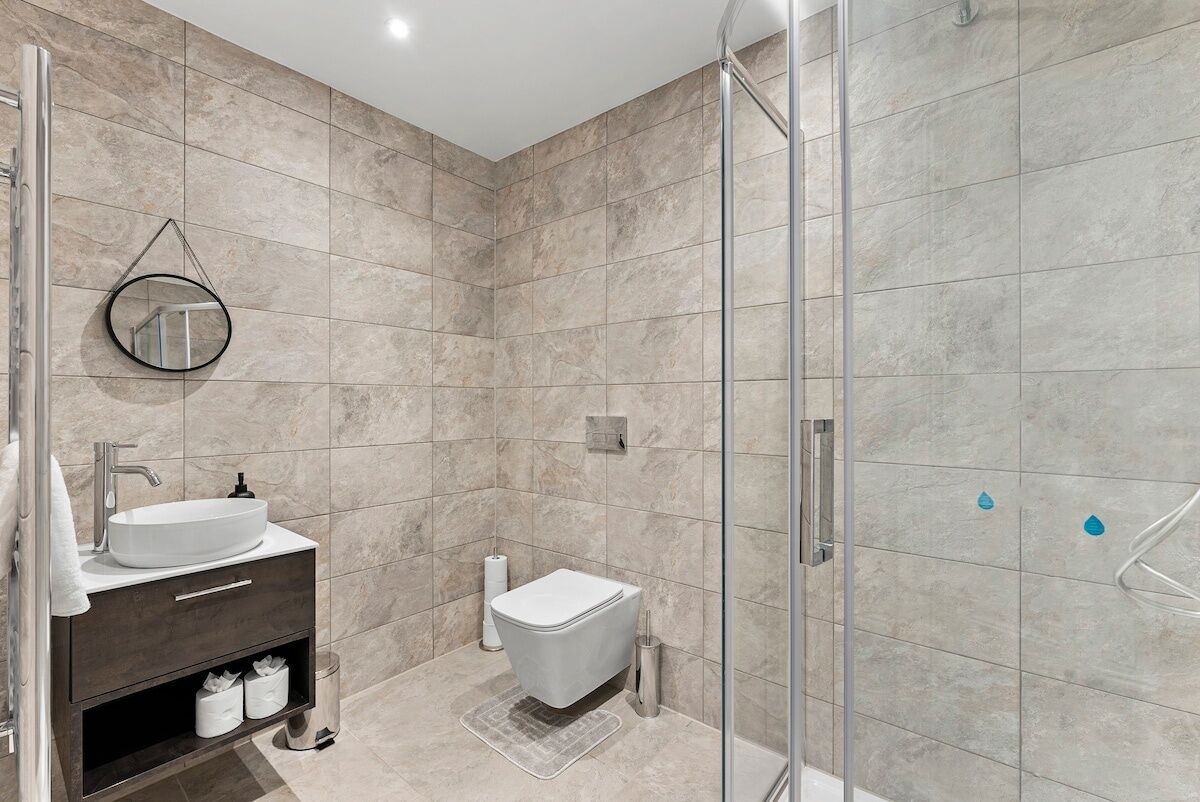 A modern bathroom with a glass-enclosed shower, a white sink, and a dark vanity.
