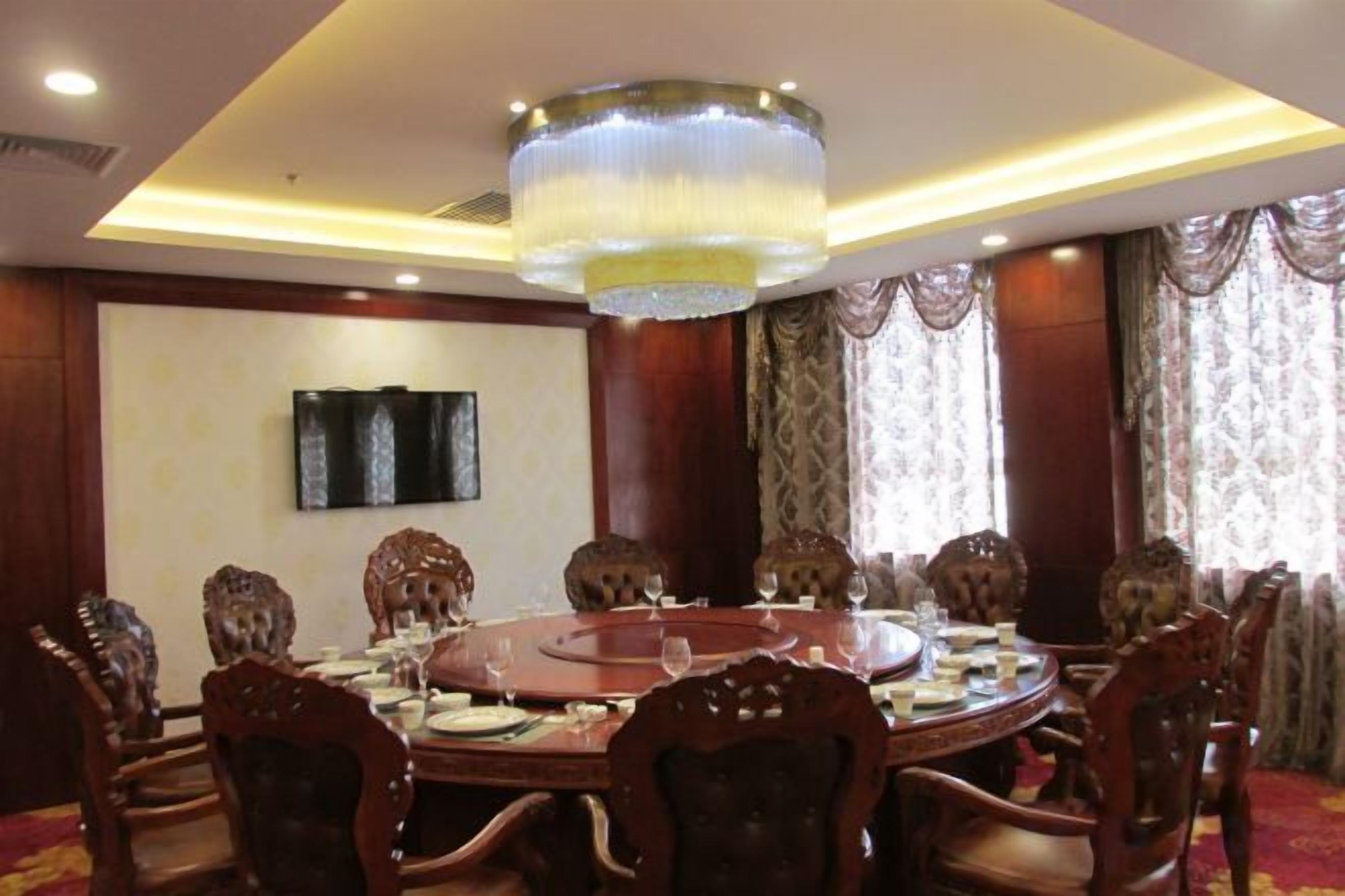 A conference room with a round table, chairs, a chandelier, and a television on the wall.