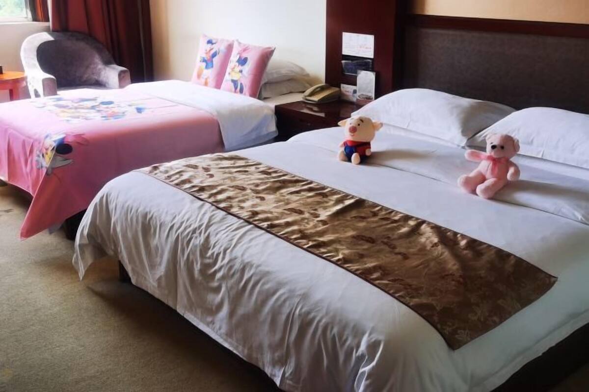 Hotellihuoneessa on kaksi sänkyä, toisessa on vaaleanpunainen päiväpeite ja toisessa valkoinen. Molemmissa sängyissä on pehmolelu, toinen on vaaleanpunainen ja toinen valkoinen.