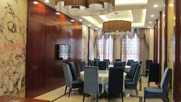 A dining area with round tables and chairs, a flat-screen TV mounted on the wall, and a chandelier.