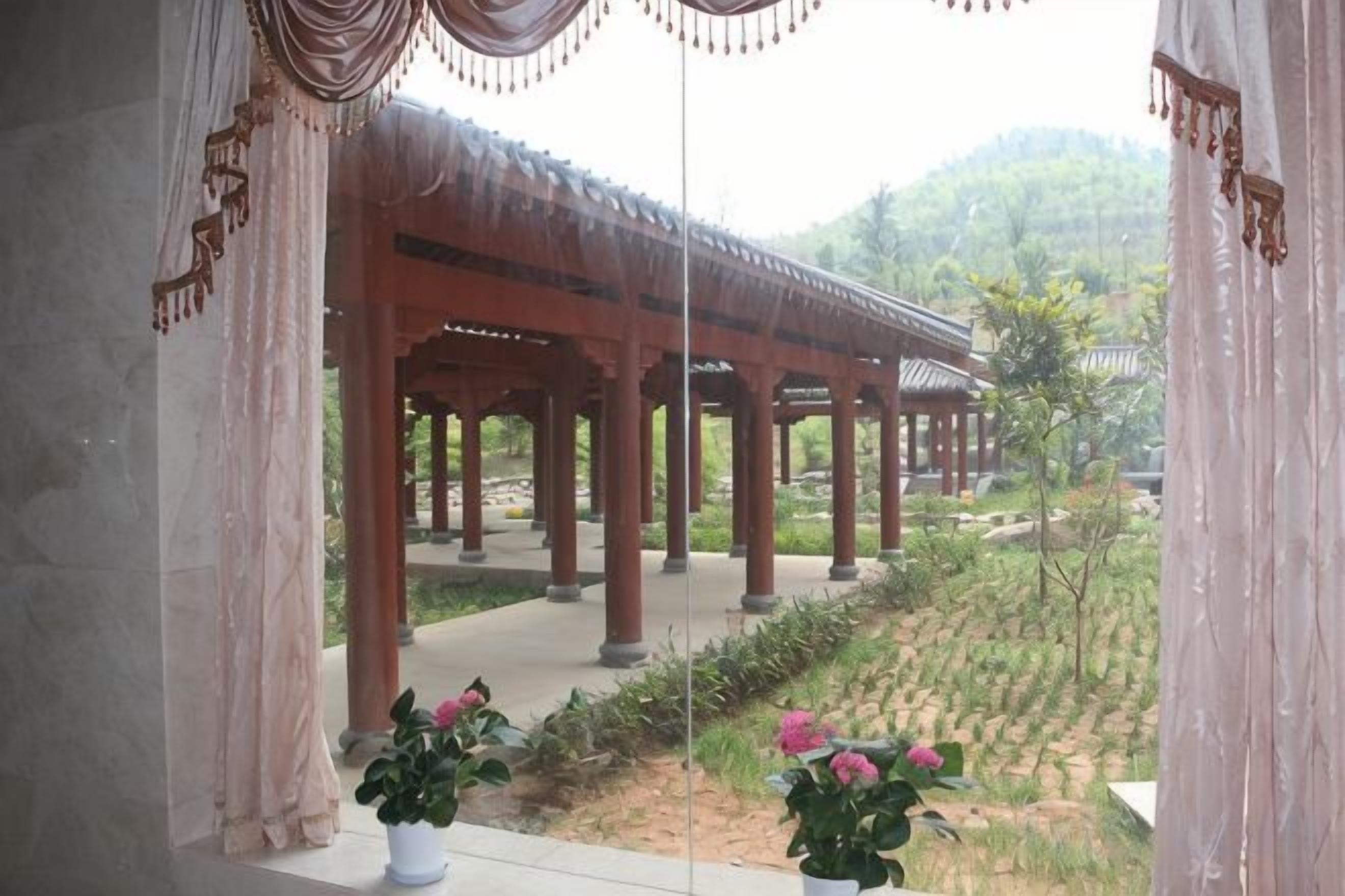 A traditional pavilion structure with multiple columns, surrounded by potted plants and a view of a hilly landscape.