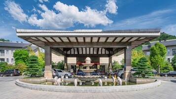 A covered pavilion with a fountain, surrounded by a parking area and trees.