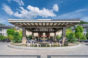 Un pavillon abrité avec une fontaine, entouré d’un parking et d’arbres.