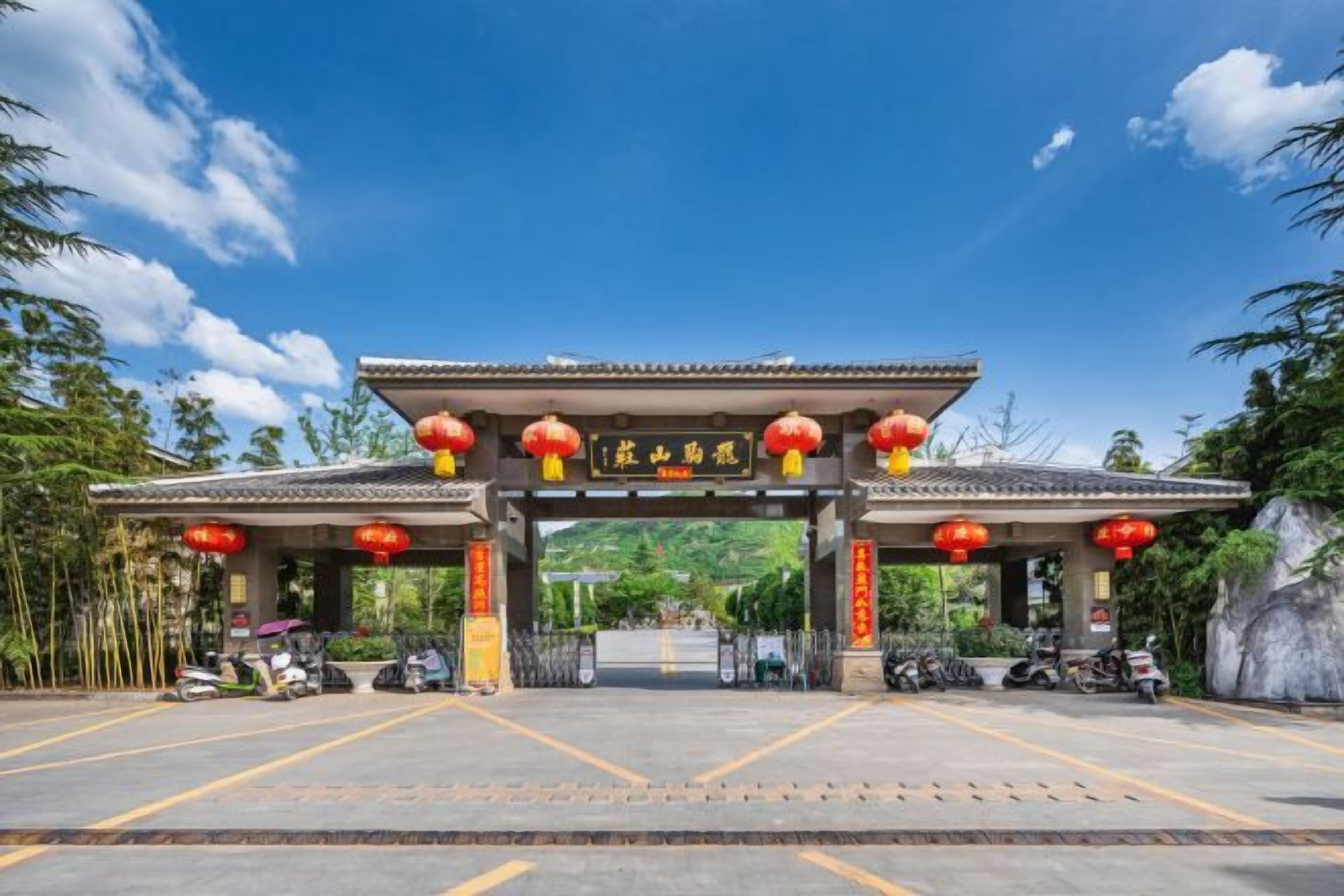 Ein traditionelles chinesisches Tor mit roten Laternen, ein klarer Himmel und ein Parkplatz mit Motorrädern.