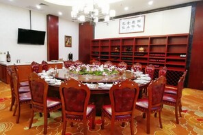 A conference room with a round table, red upholstered chairs, a chandelier, a television on the wall, and a wine rack. - Jinshan Hotel (Danfeng)