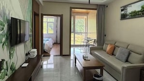 Camera d'albergo con TV, divano, tavolino da caffè, un quadro e vista sull'esterno.