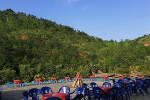 An outdoor seating area with tables and chairs, surrounded by a forested hillside. - Jinshan Hotel (Danfeng)