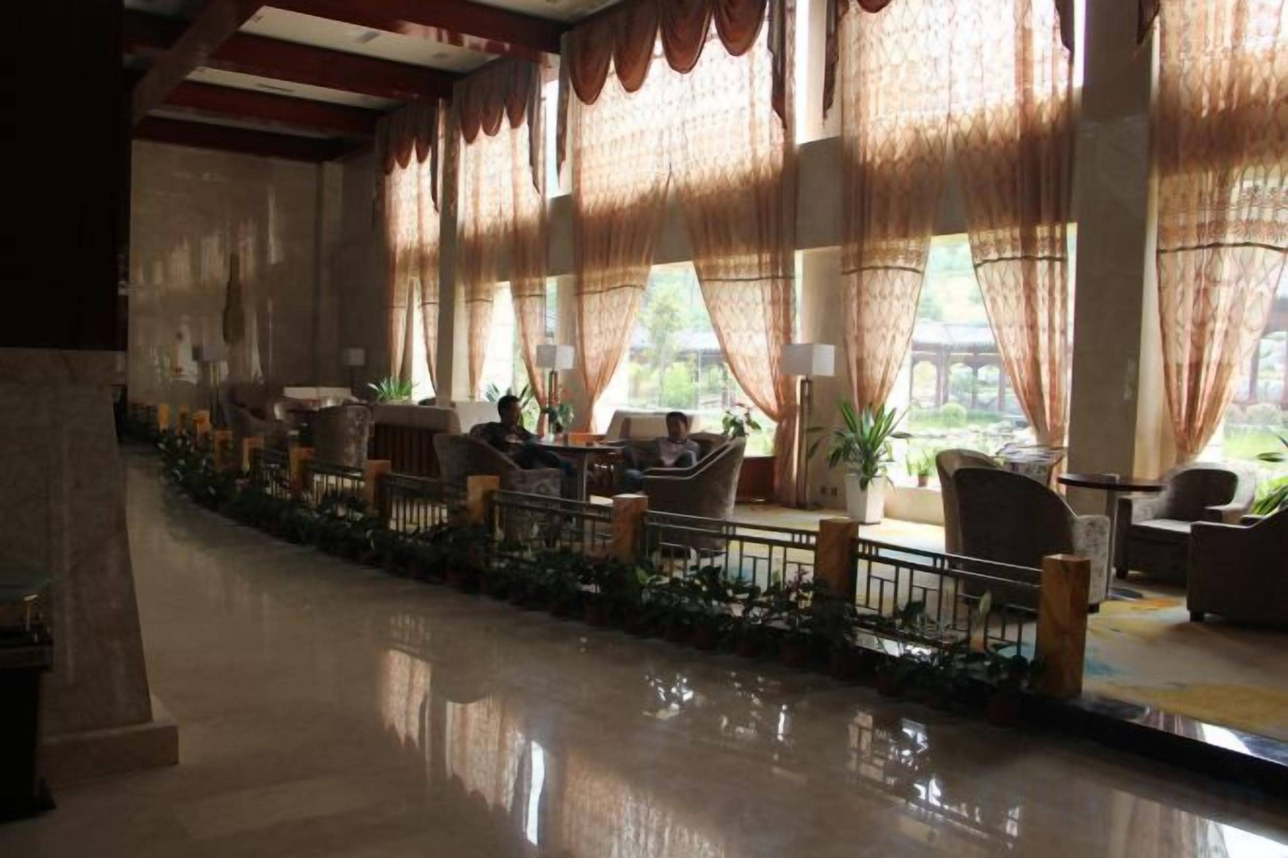 A hotel lobby with a long, reflective floor, rows of seating, and large windows with curtains.