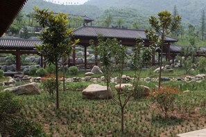 A traditional pavilion with a tiled roof, surrounded by a landscaped garden with various plants and rocks. - Jinshan Hotel (Danfeng)