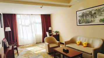 A hotel room with a sofa, armchairs, a coffee table, and a painting on the wall.