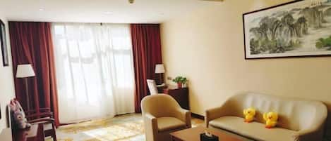 A hotel room with a sofa, armchairs, a coffee table, and a painting on the wall.