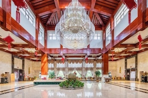 Een ruime lobby met een grote kroonluchter, houten balken en een opvallend decoratief middelpunt.