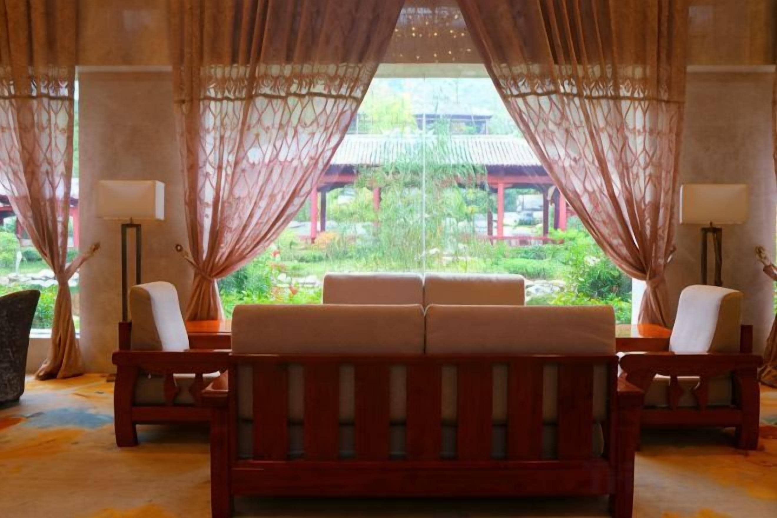 Une pièce avec un canapé et des fauteuils, disposés de manière à offrir une vue sur un bâtiment traditionnel et un jardin.