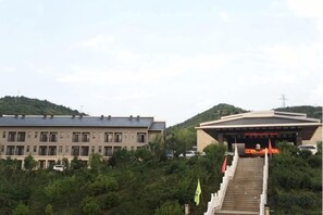 A building with a staircase leading to a covered entrance, surrounded by greenery. - Jinshan Hotel (Danfeng)