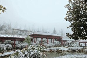 Un jardín tradicional japonés con un estanque, plantas cubiertas de nieve y estructuras de techo rojo.