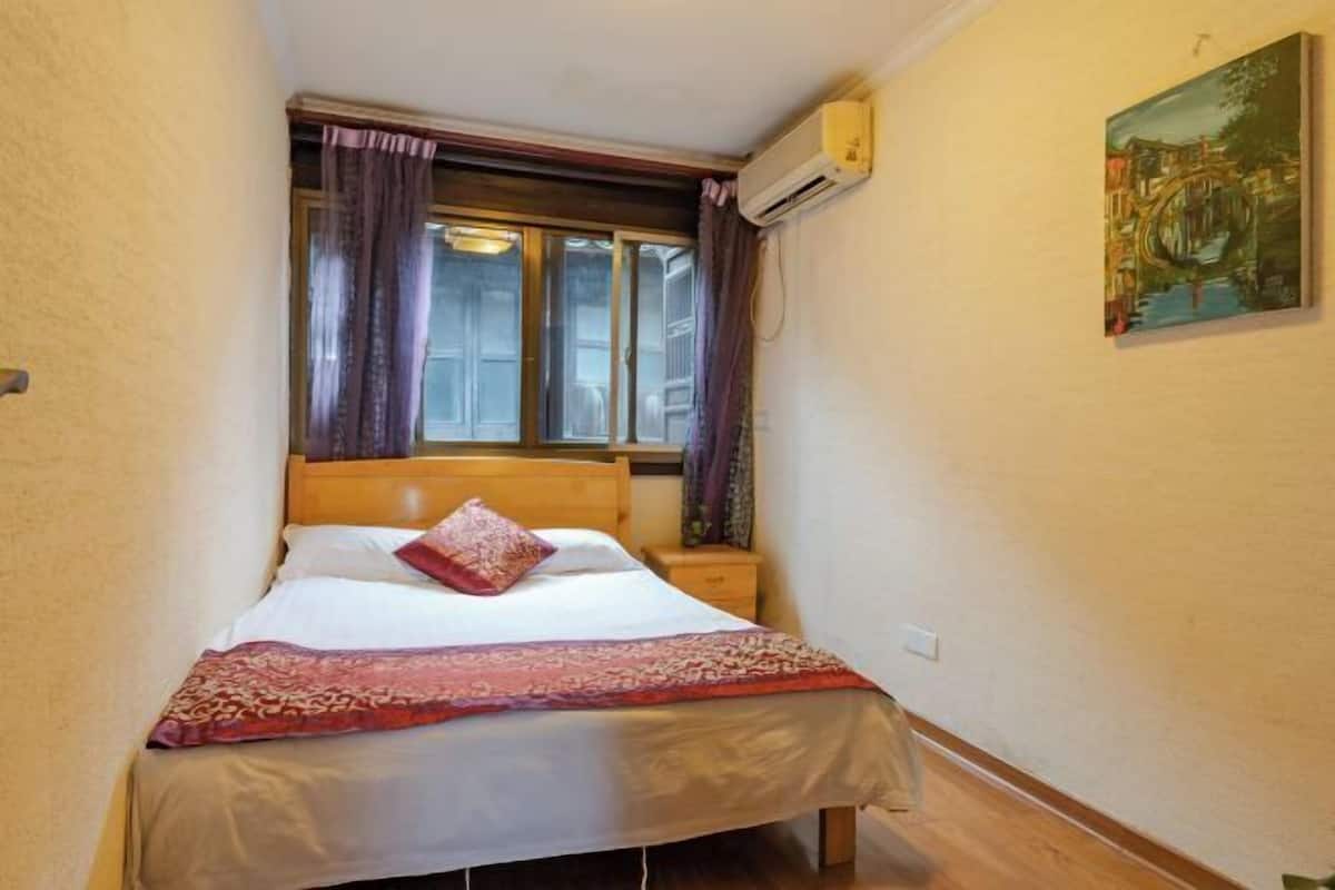 Um quarto pequeno e acolhedor com uma cama de solteiro, uma mesa de cabeceira, uma janela com cortinas e um ar condicionado fixado na parede.