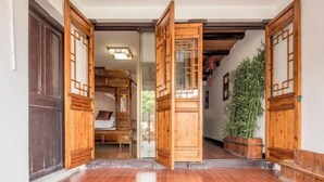 Μια παραδοσιακή ξύλινη πόρτα με ένα συρόμενο γυάλινο τμήμα, ένα πλακόστρωτο δάπεδο και ένα φυτό σε γλάστρα.