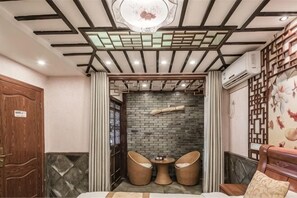 Una habitación con puerta de madera, pared de ladrillo, techo con diseño geométrico y dos sillas de mimbre.