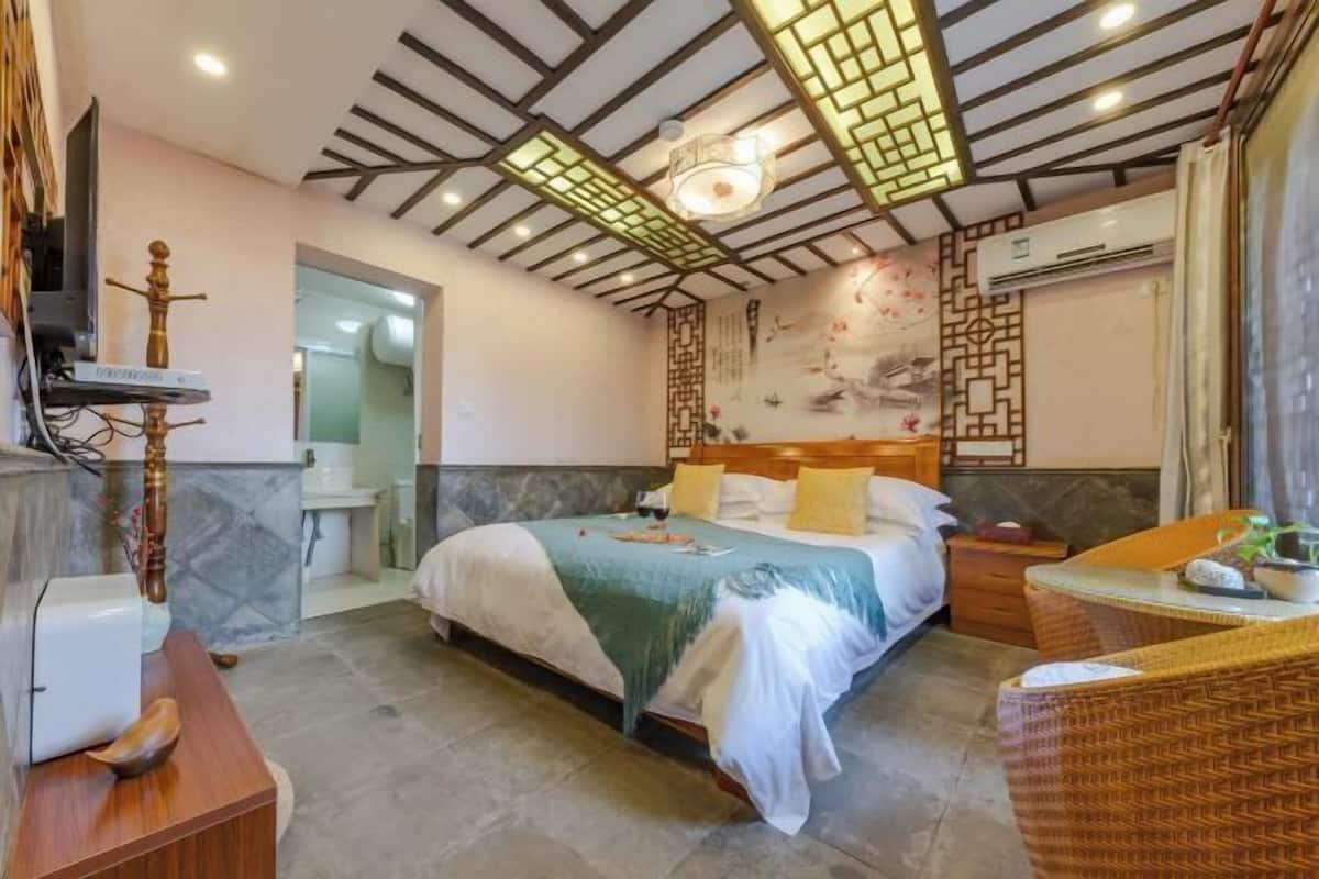 Quarto com cama, mesa de cabeceira e um pequeno espaço de estar com uma poltrona.
