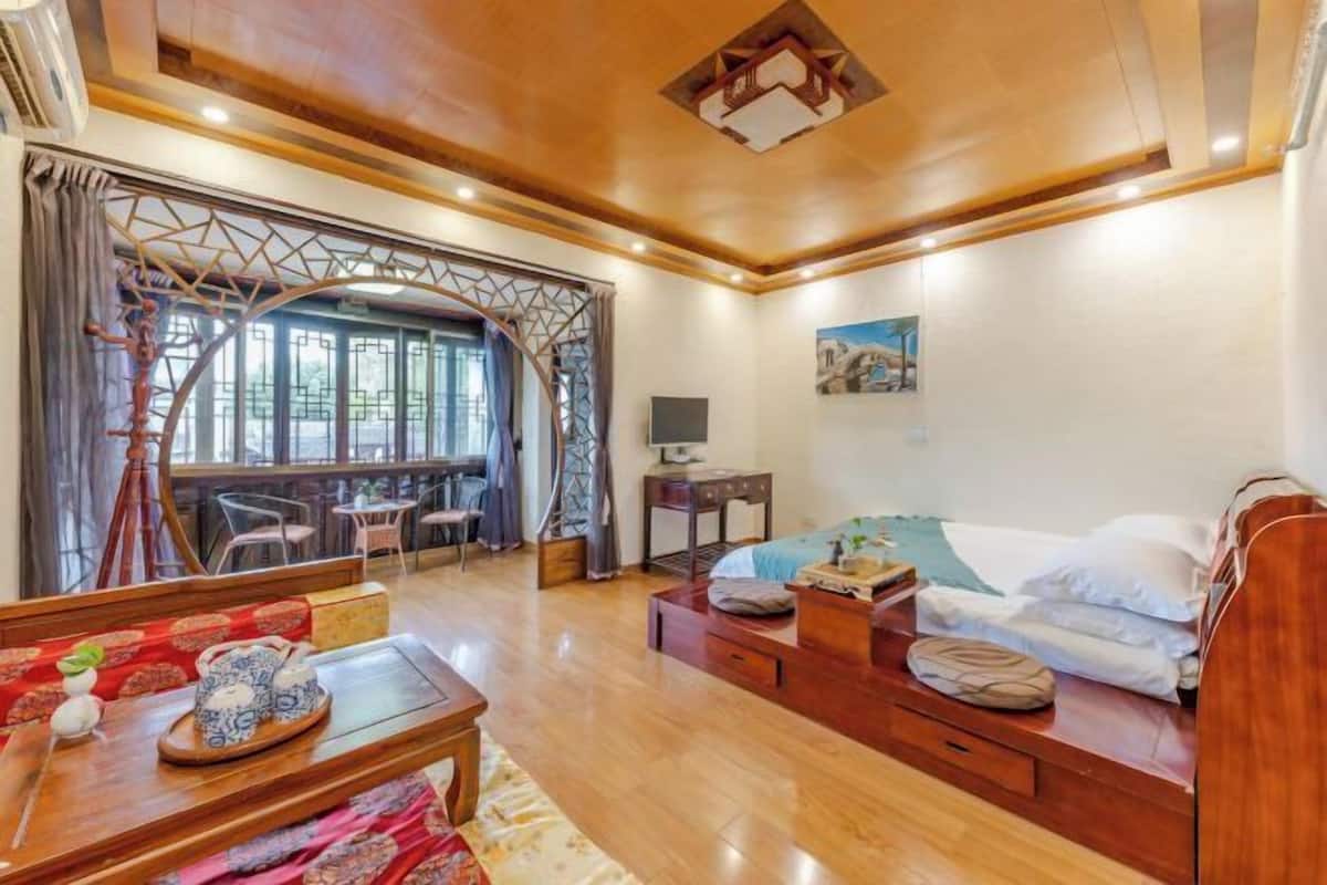 Quarto com teto de madeira, cama, escrivaninha e área de estar com mesa e cadeiras.