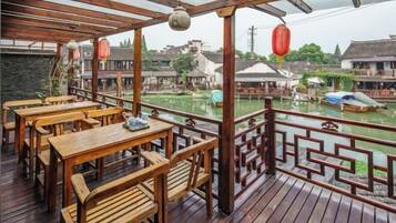 A wooden deck with tables and chairs overlooking a canal with traditional buildings.