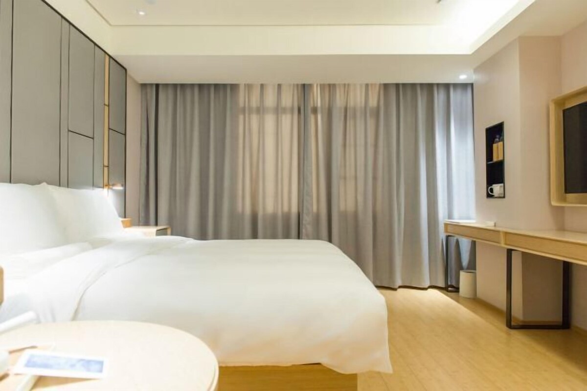 A modern hotel room with a bed, a desk, and a large window with curtains.