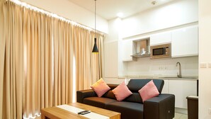 A modern living room with a sofa, a coffee table, and a kitchen area in the background. - suncity Apartments (Accra)