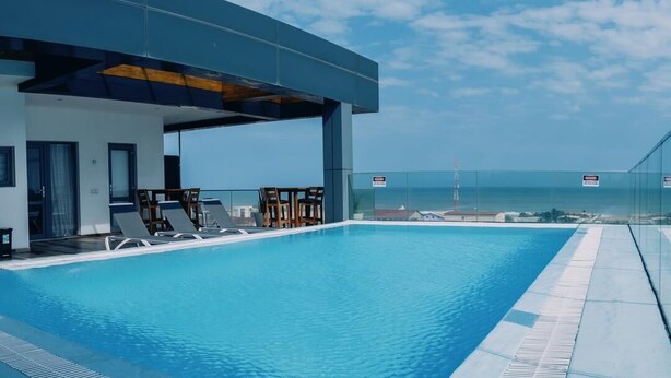 A rooftop infinity pool with lounge chairs and a glass railing overlooking the ocean. - suncity Apartments (Accra)