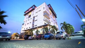 A multi-story hotel with a modern design, featuring balconies on each floor, a covered entrance, and a parking area with several cars. - suncity Apartments (Accra)