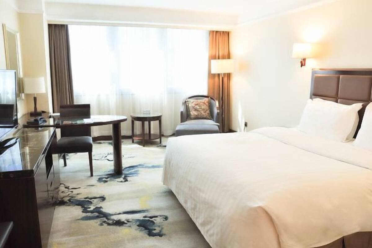 A hotel room with a large bed, a desk with a chair, a small table, and a television.