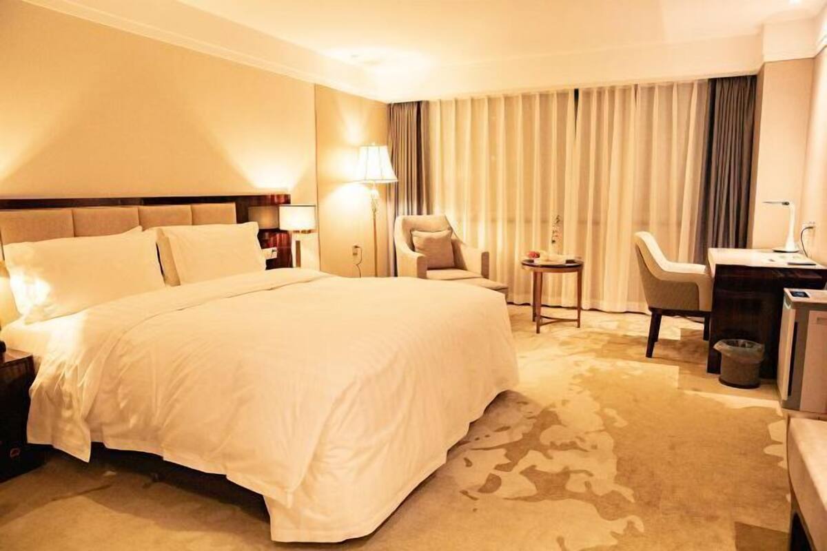 A hotel room with a large bed, a desk, a chair, and a small table.