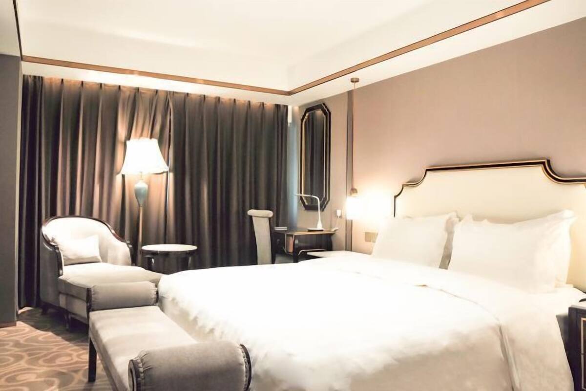 A hotel room with a large bed, a chair, a desk, a lamp, and a mirror.