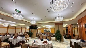 Un comedor de hotel con mesas redondas, sillas, candelabros y un gran pilar decorado con una planta.