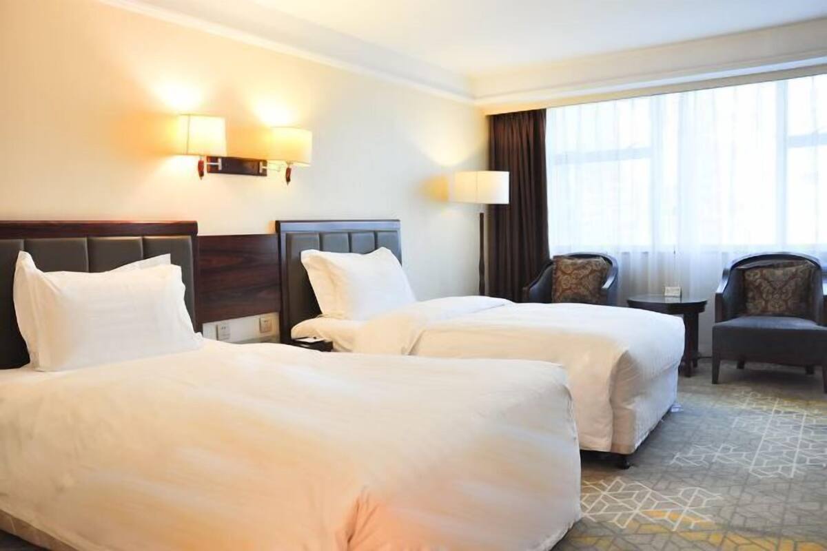 A hotel room with two beds, a small table, two chairs, and a large window with curtains.