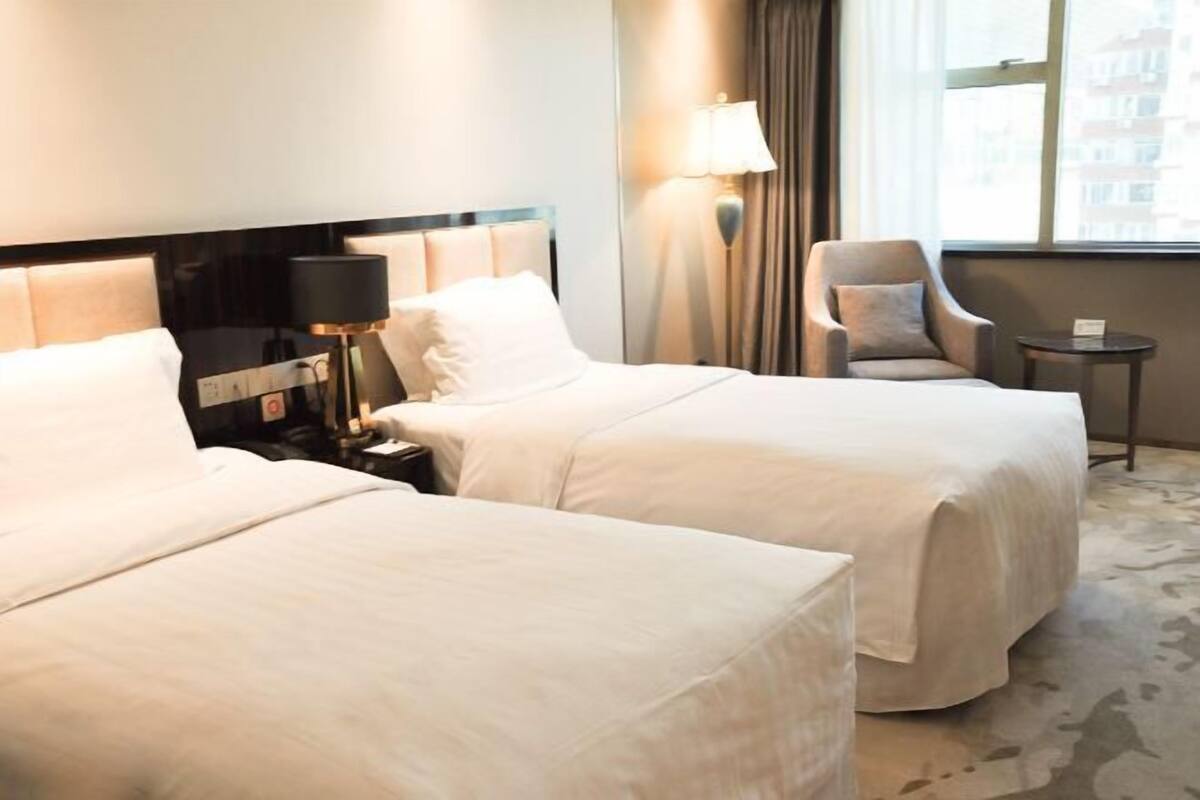 A hotel room with two beds, a nightstand with a lamp, a chair, and a small table.