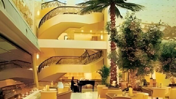 Un amplio vestíbulo de hotel con varios niveles, una imponente escalera, zonas de estar y un piano.