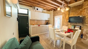 Una cocina moderna con armarios blancos, un comedor con sillas blancas y una pared de ladrillo.