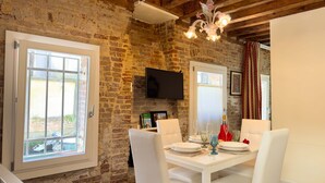 Un comedor con pared de ladrillo, un televisor de pantalla plana y una mesa para dos con sillas blancas.