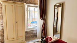 Una habitación con un armario grande, una ventana con barrotes, un espejo y un ventilador rojo y blanco en el suelo.