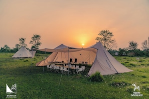 Un camping con varias tiendas de campaña, una mesa de comedor con sillas y una vista despejada del atardecer.