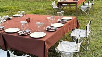 An outdoor dining setup with tables set for meals, surrounded by tents in a grassy field.