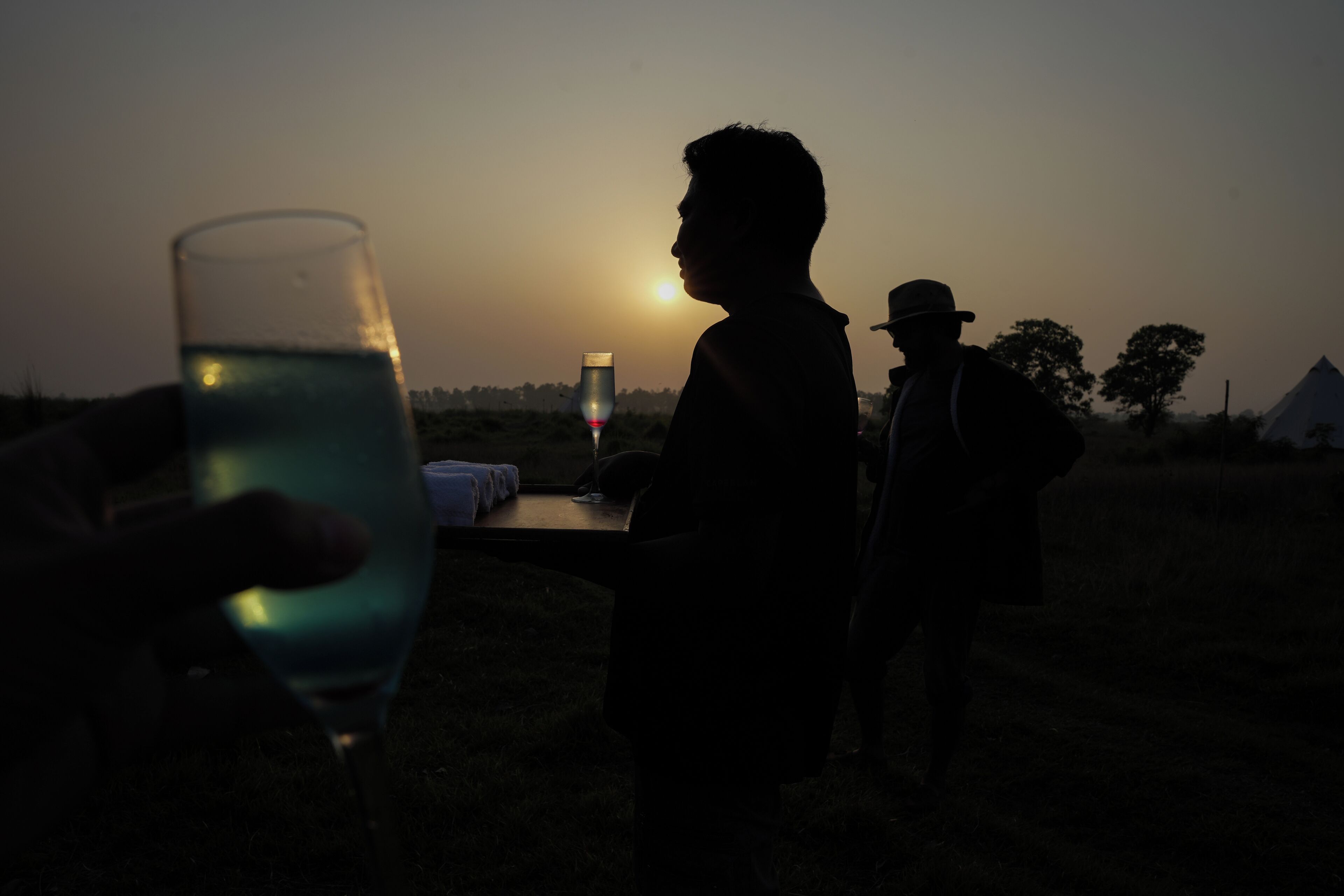 A silhouette of a person holding a glass, with a sunset in the background.