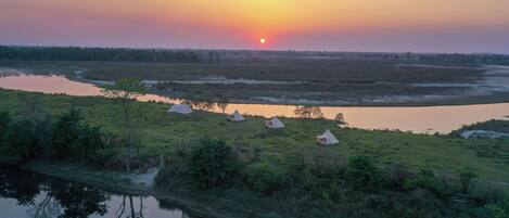 A sunset over a river with tents and greenery.