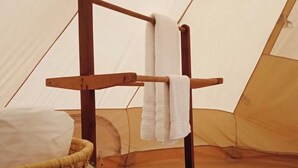 A tent interior with a wooden rack holding towels, a woven basket, and a mattress on the floor. - Burhan Wilderness Camps (Manjhara)