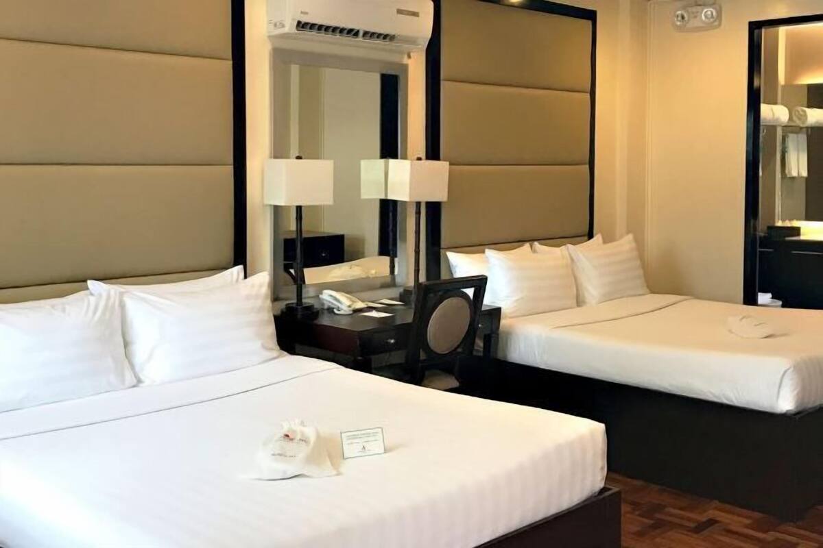 Una habitación de hotel con dos camas individuales, una mesita de noche con lámpara, un espejo y un equipo de aire acondicionado.