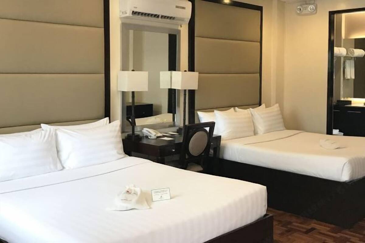 Una habitación de hotel con dos camas individuales, una mesita de noche con lámpara, un espejo y un aire acondicionado de pared.